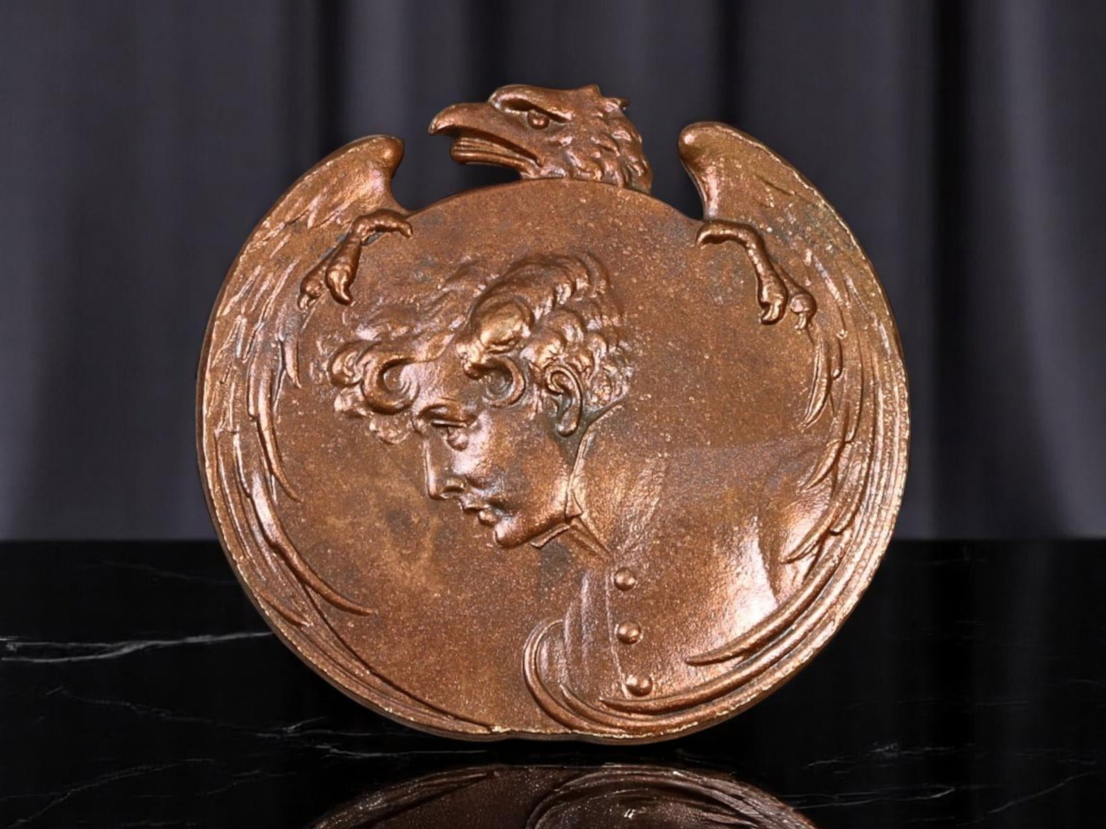ART NOUVEAU: Bronze Medallion - Youthful Profile & Eagle Emblem, Patinated Finish (2.5cm): Evocative of early 20th-century artistry, this finely cast Art Nouveau medallion features a striking youth's profile under the protective embrace of a stylized eagle. The piece bears a mellow bronze p