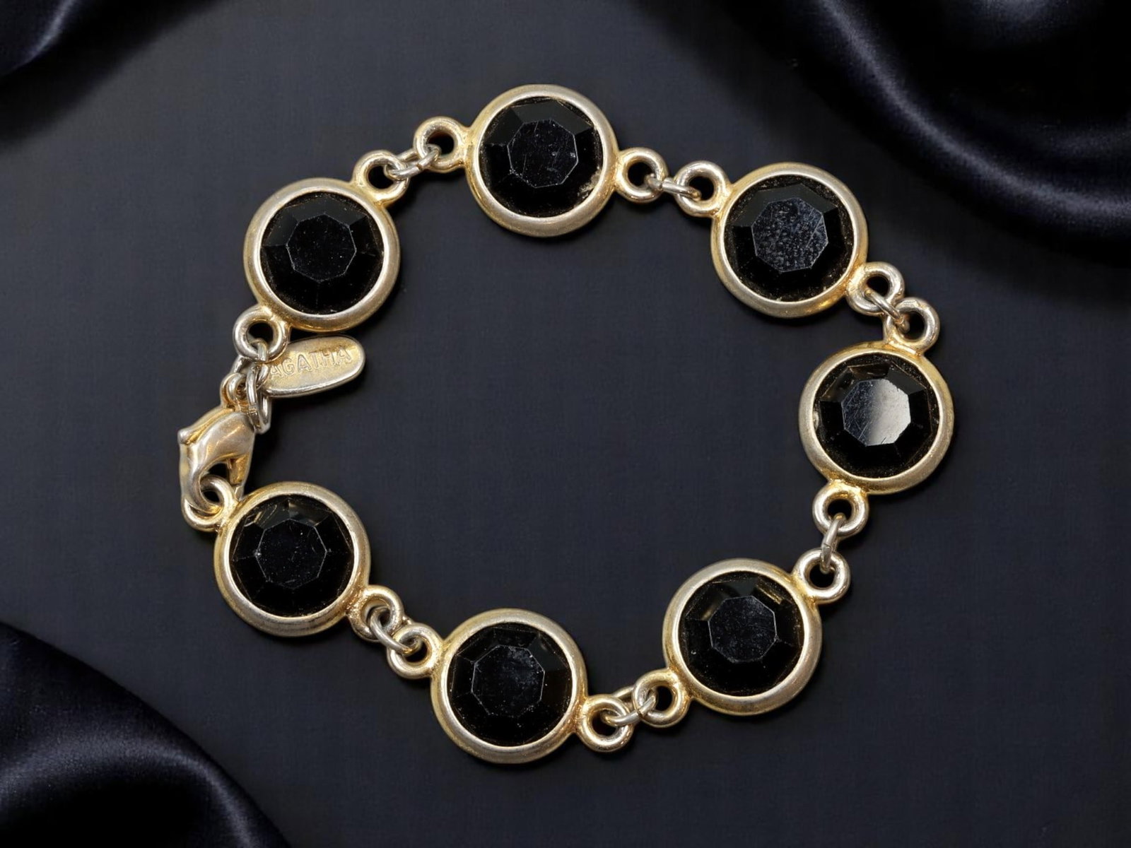 FRENCH DESIGNER AGATHA Paris Link Bracelet - Faceted Jet-Style Cabochons, 16.3 cm: A refined designer piece from Agatha Paris, this bracelet features seven bezel-set, faceted black cabochons linked in a continuous circle. Framed in a warm goldtone finish, the bold contrast of the je