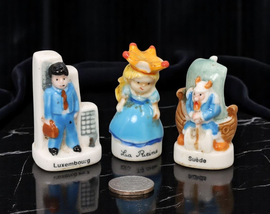 FRENCH: Feve Trio - Luxembourg, Sweden & Fairytale Queen, Hand-Glazed Porcelain (3 pcs, 3-3.5 cm): A whimsical trio of contemporary French feves highlighting national and fantasy motifs through vibrant hand-glazed porcelain. This set includes a suited businessman labeled 'Luxembourg,' posed in fron