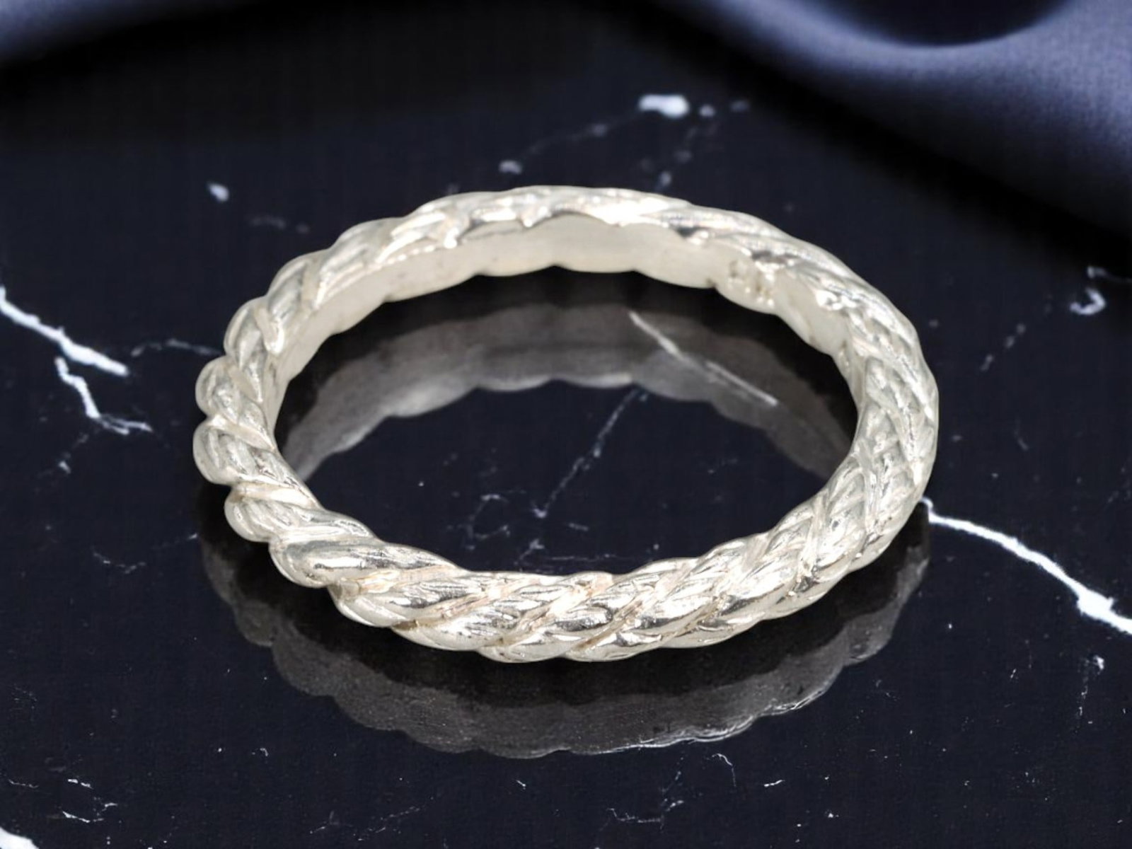 BR ARTISAN: Ring - Braided Rope Motif Band, Silvertone Finish, Size 6 US: This distinctive contemporary ring by BR features a continuous braided rope motif encircling the band. Crafted with a richly textured silvertone finish, the design offers sculptural dimension and tact