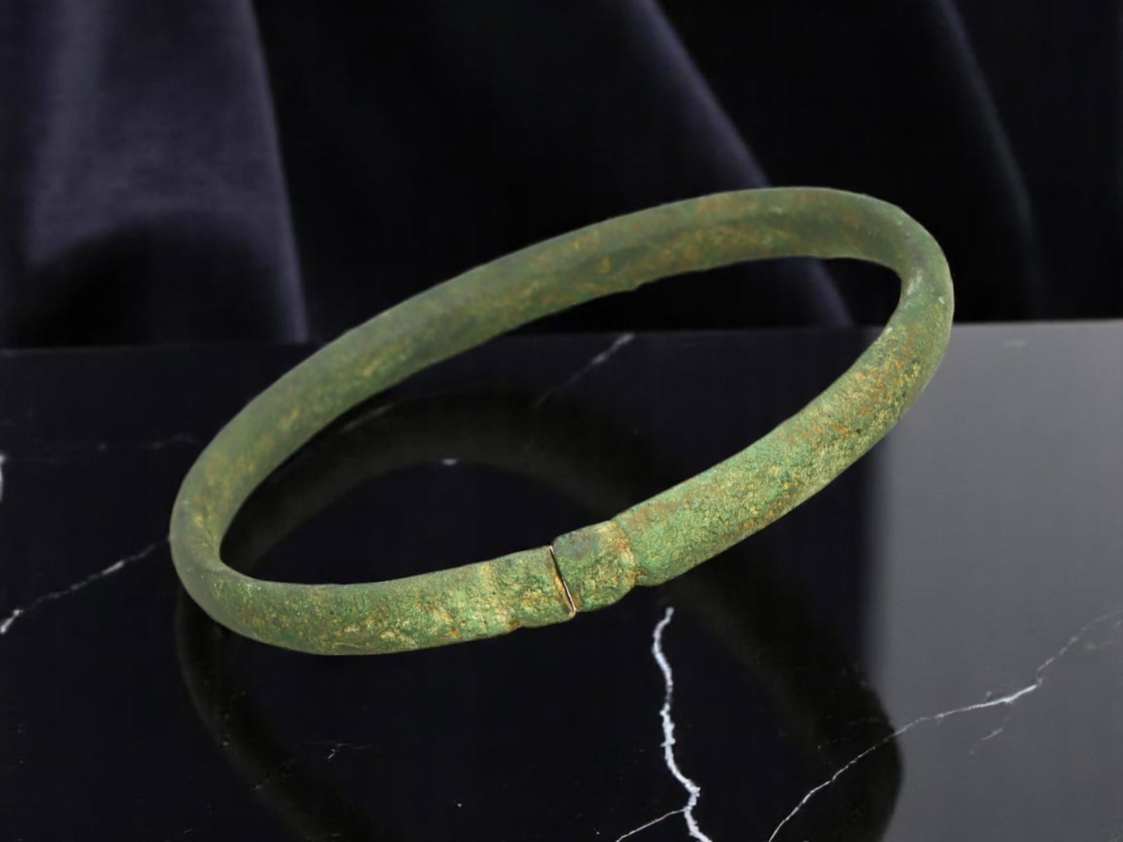 LATE ROMAN / EARLY BYZANTINE Central-Ridge Bronze Bracelet, 5.7 cm: This small, closed bronze bracelet is defined by a central raised ridge motif that mimics a clasp, subtly segmenting the otherwise smooth circular band. Its compact diameter and minimal ornamentation 