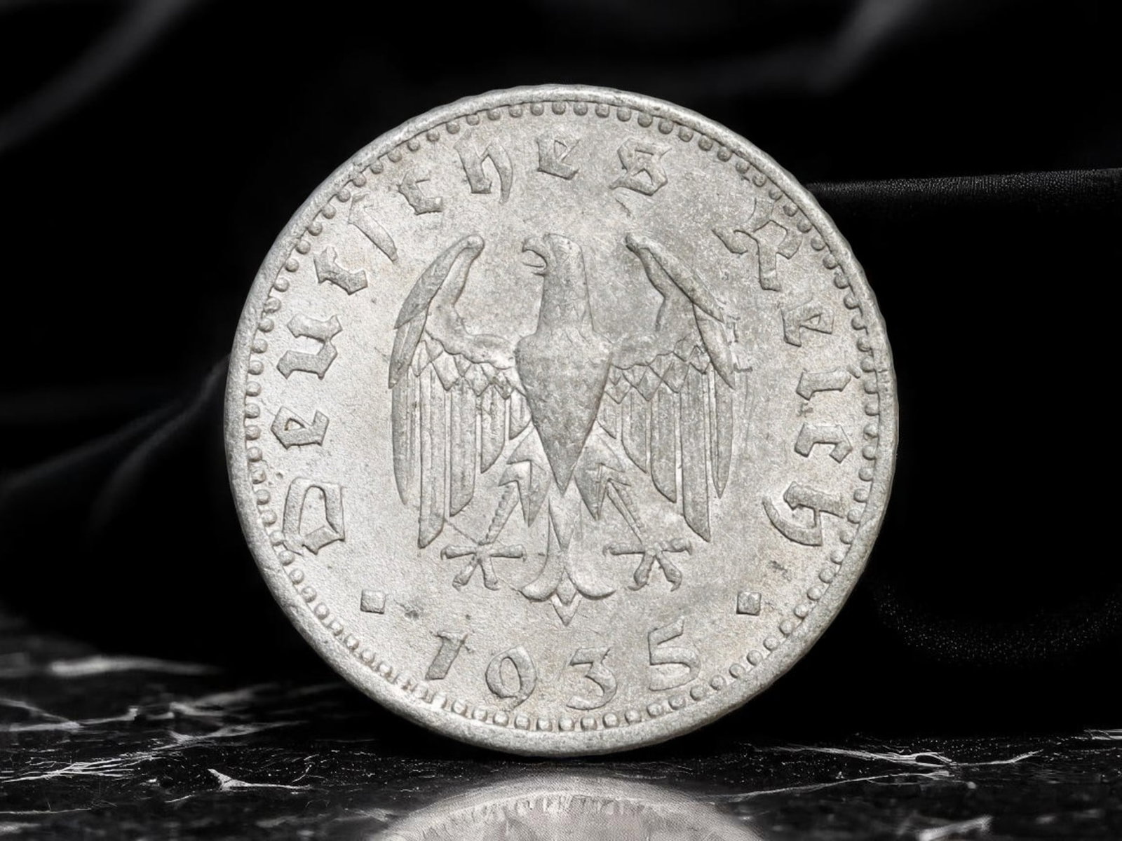 GERMANY/THIRD REICH: Reichsadler 50 Reichspfennig Coin, 1935 A Berlin Mint, 23mm: Minted in 1935 under the rising grip of authoritarianism, this 50 Reichspfennig coin illustrates the early propaganda efforts of the Third Reich through numismatic design. The obverse displays the sty