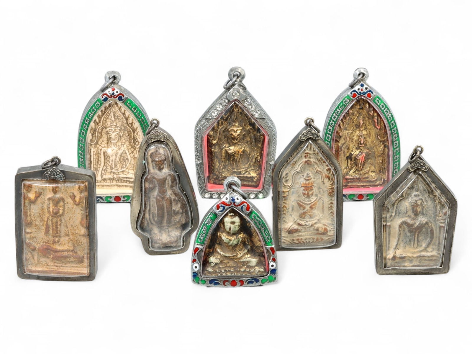 Antique Thai Buddhist Iconography Clay Amulets in Silver-Enamel Cases, Early 20th Century, 342g: This captivating ensemble of seven antique Thai Buddhist amulets represents a unique convergence of religious devotion, traditional clay craftsmanship, and ornamental artistry. Each amulet, carefully