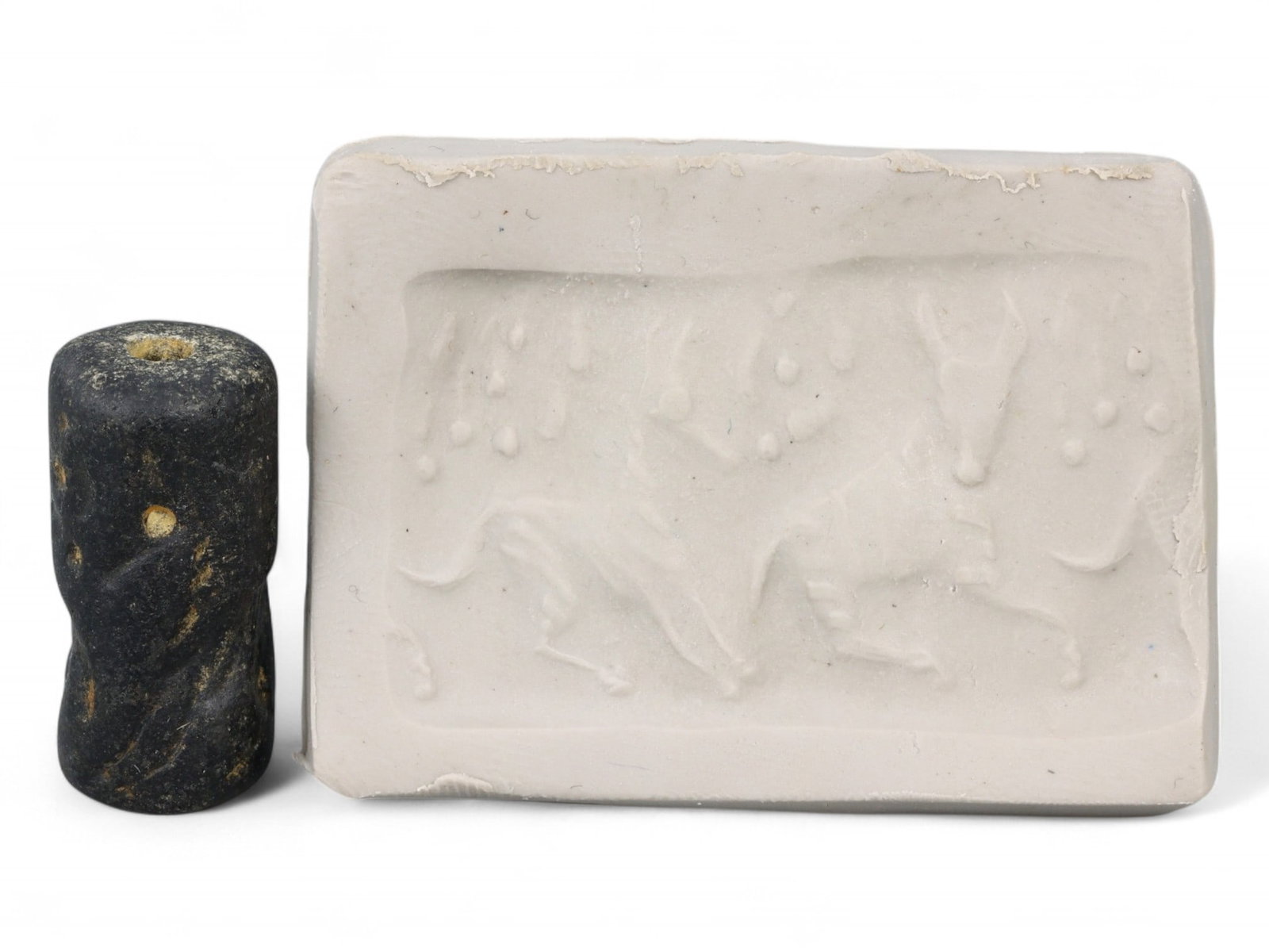Ancient Akkadian Leaping Ibex Cylinder Seal in Black Stone, c. 23rd-22nd Century BCE, 6g: This rare Akkadian cylinder seal, carved from deep black stone rather than the more common lapis lazuli, depicts a dynamic scene of two leaping ibexes framed by a constellation of dotted motifs-likely