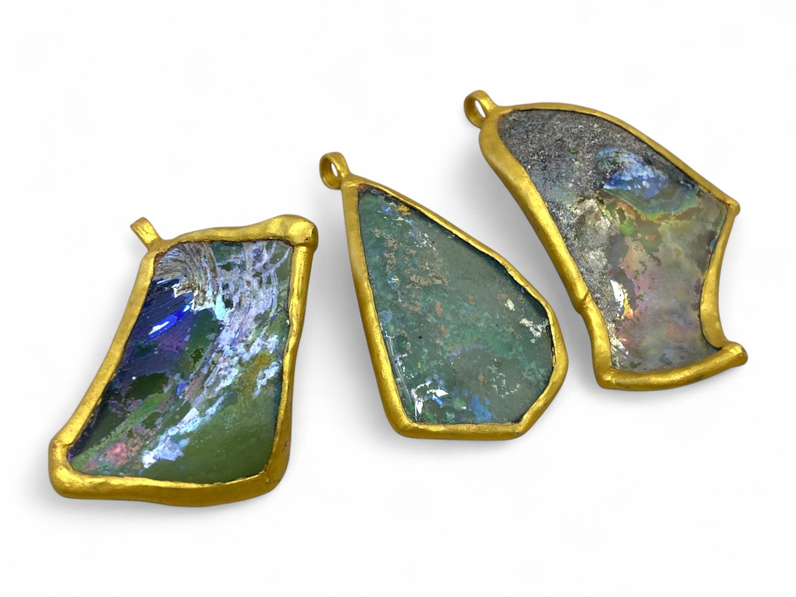 Ancient Roman Iridescent Glass Pendants in Modern Gilt Settings, Glass c. 1st-3rd Century CE, 55g: This striking trio of pendants features authentic fragments of ancient Roman glass, dating from the 1st to 3rd century CE, masterfully set in modern gilt frames. Each pendant measures between 6 to 7 c