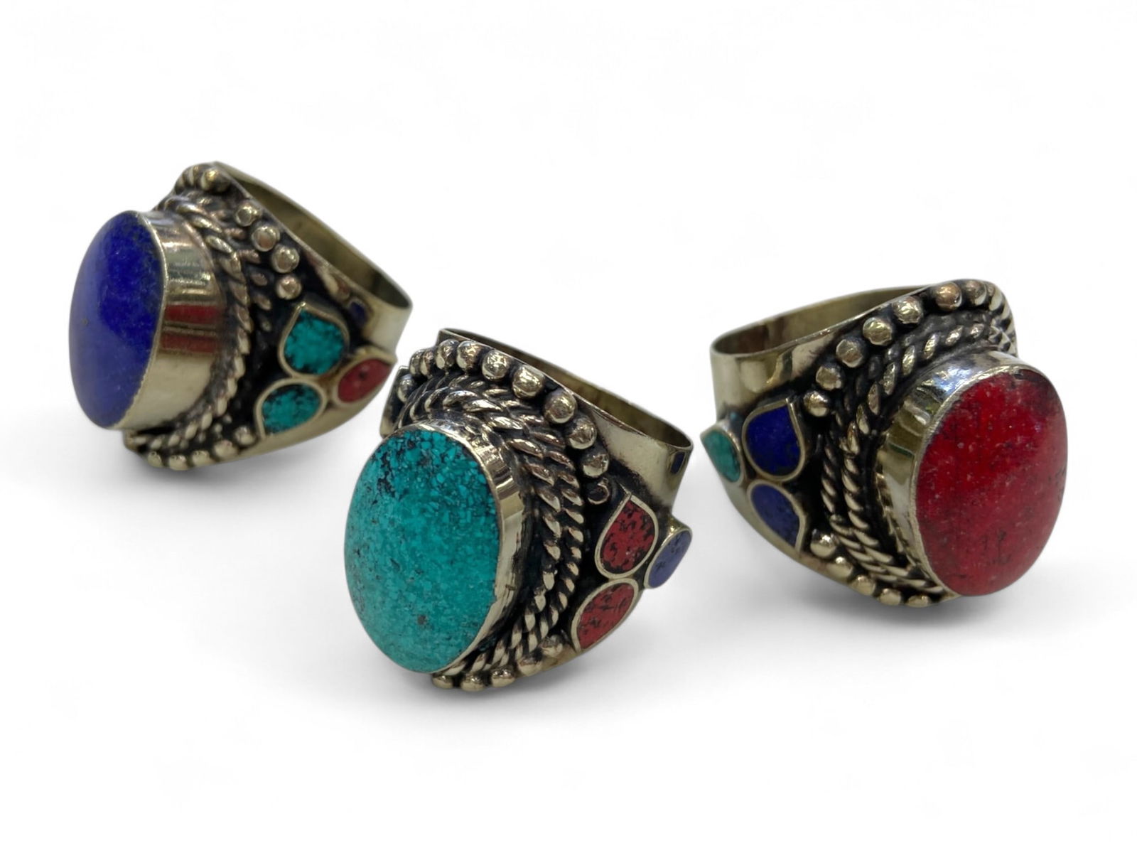 Tribal Inlay Statement Rings Lot with Turquoise, Coral, and Lapis, 3 Rings, 94g: This vibrant lot of three handcrafted tribal rings embodies the bold aesthetic and spiritual symbolism of Himalayan or Central Asian jewelry traditions. Each ring features a large domed cabochon-turqu
