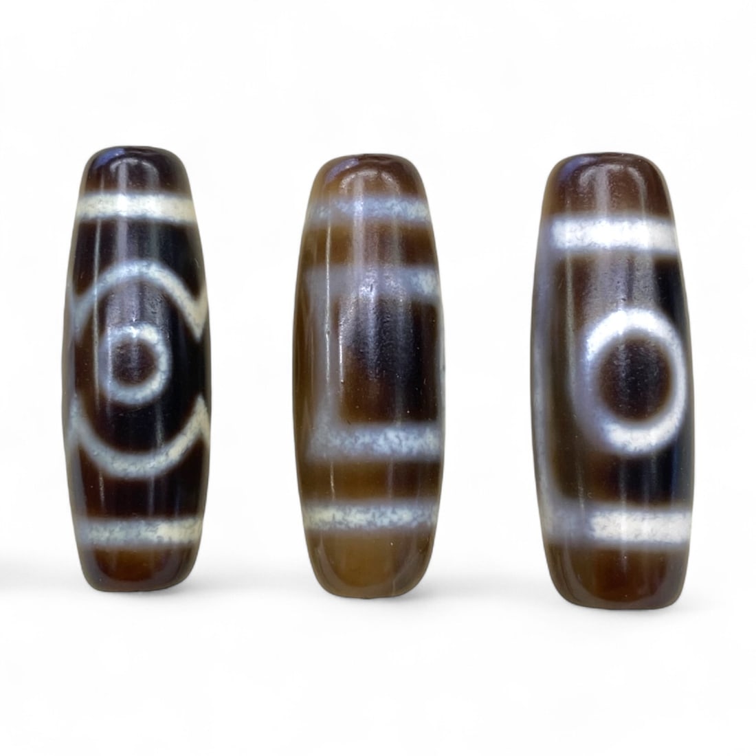 Lot of Tibetan Chung Dzi Beads, 3cm: This lot of Tibetan Dzi beads features the traditional etched agate designs prized for their protective and spiritual qualities. Each bead is cylindrical, displays crisp white patterns against a deep 