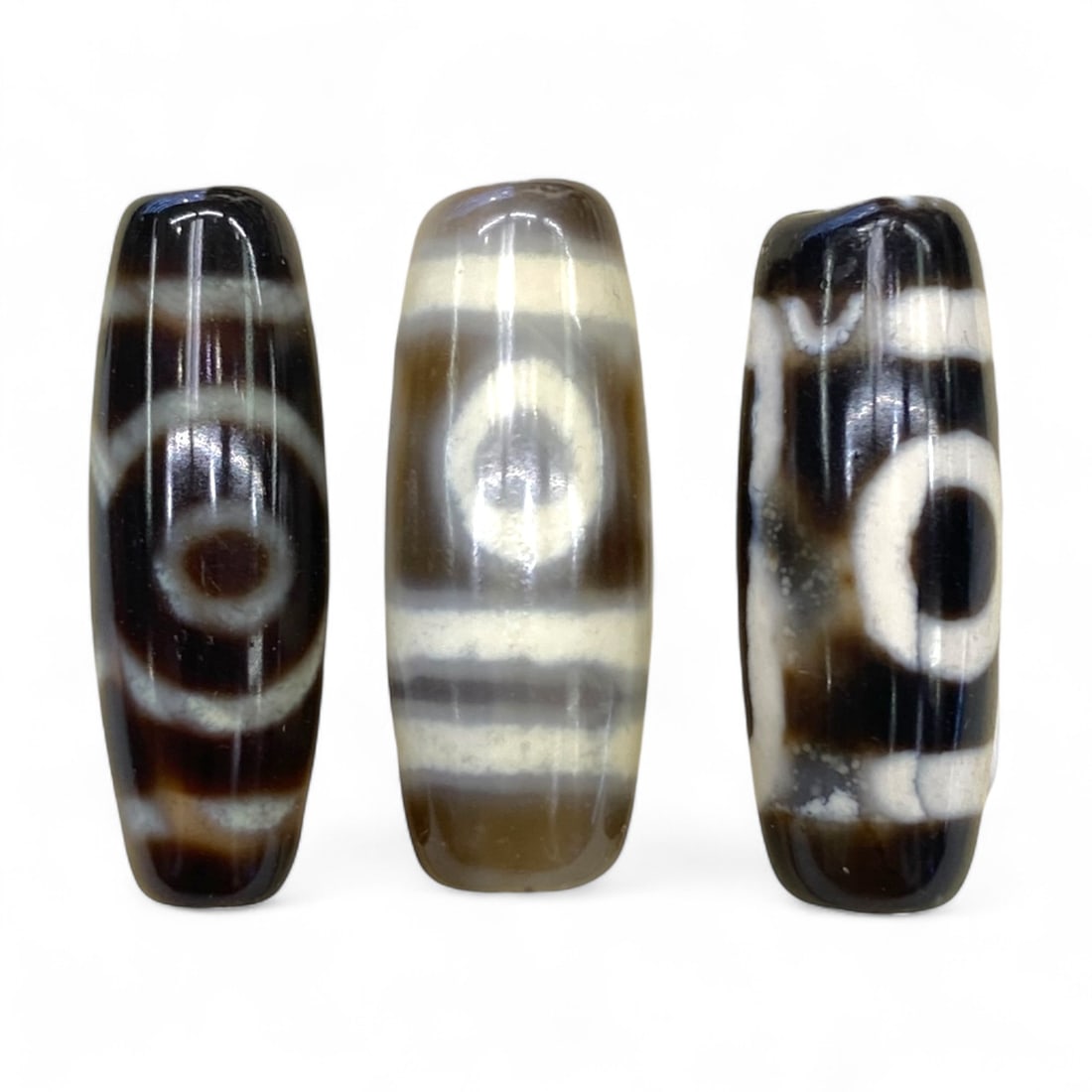 Lot of Tibetan Chung Dzi Beads, 3cm: This lot of Tibetan Dzi beads features the traditional etched agate designs prized for their protective and spiritual qualities. Each bead is cylindrical, displays crisp white patterns against a deep 