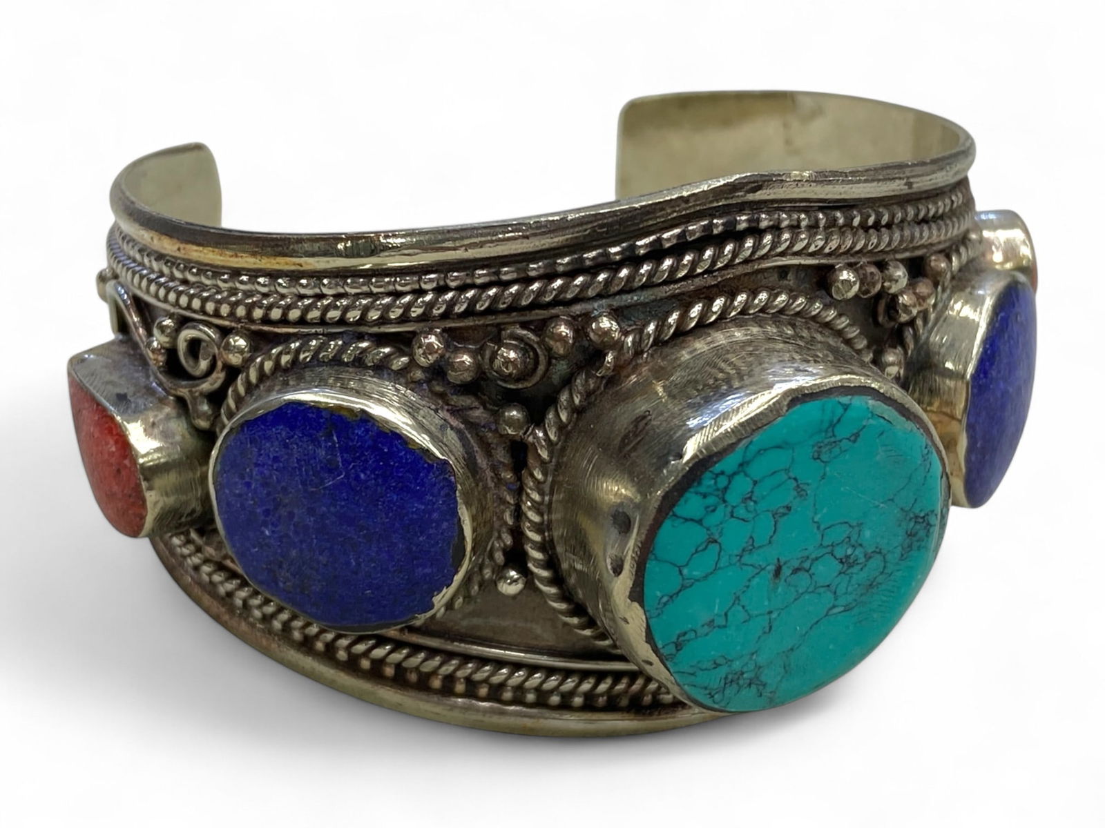 Tibetan Silver Ritual Cuff with Turquoise-Lapis-Coral Cabochons, c. 20th Century, 137g: This commanding Himalayan cuff bracelet, crafted in the 20th century, reflects the enduring power and visual symbolism of Tibetan ritual jewelry. Set in a thick silver alloy frame with bold repousse w