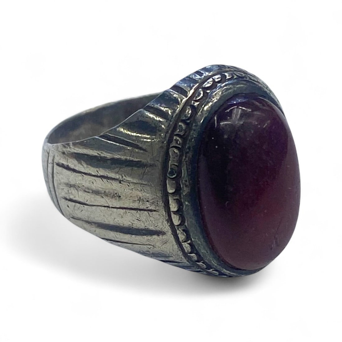 Antique Mid-20th Century Silver Ring with Deep Burgundy Cabochon and Textured Shoulders, 7g: This vintage silver ring features a smooth, oval deep burgundy cabochon set within a beaded-edge bezel. The shoulders display linear, radiating grooves that add dimension and visual flow toward the ce