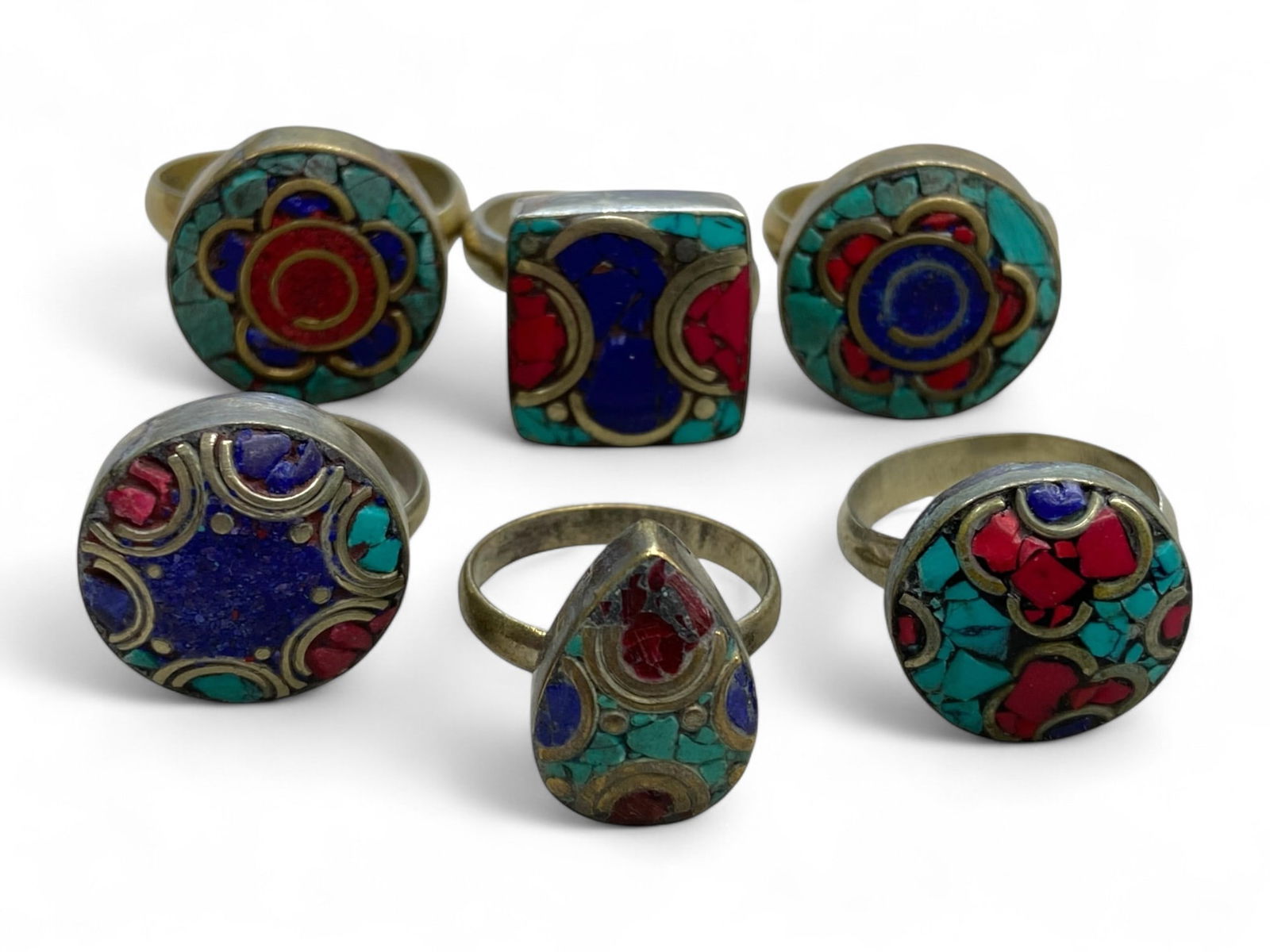 Vintage Himalayan Tribal Turquoise Coral Lapis Mosaic Rings, 20th Century, 31g: This set of six vintage Himalayan rings exemplifies the bold artistry of tribal jewelry, with each piece showcasing intricate stone mosaics set in brass-toned mounts. Turquoise, coral, and lapis lazul