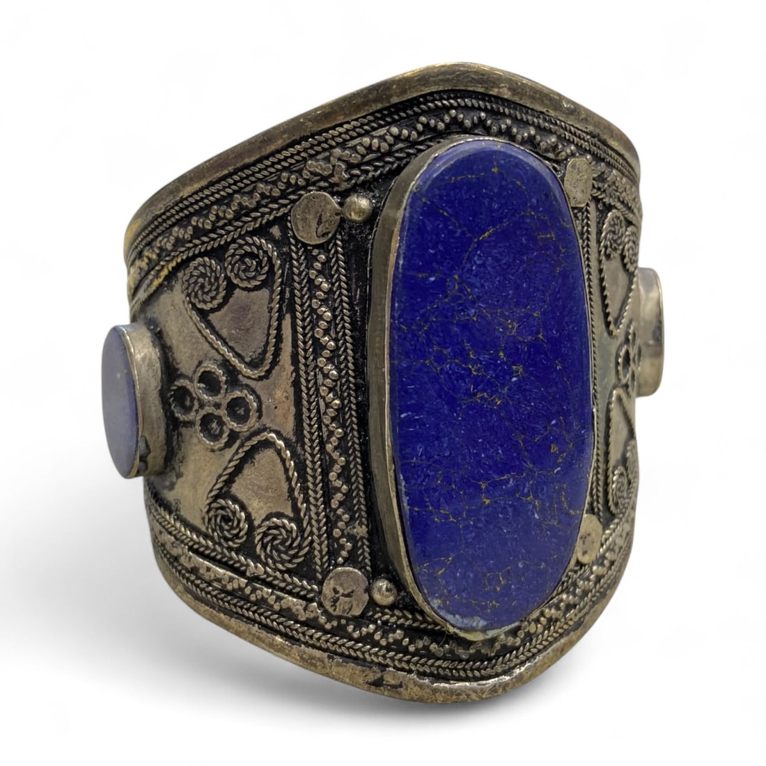 Vintage Himalayan Tribal Lapis Lazuli Silver Bracelet, 20th Century, 57g: This vintage Himalayan bracelet showcases the deep celestial beauty of lapis lazuli, set in a broad silver cuff richly adorned with traditional repousse patterns. The centerpiece is a striking elongat