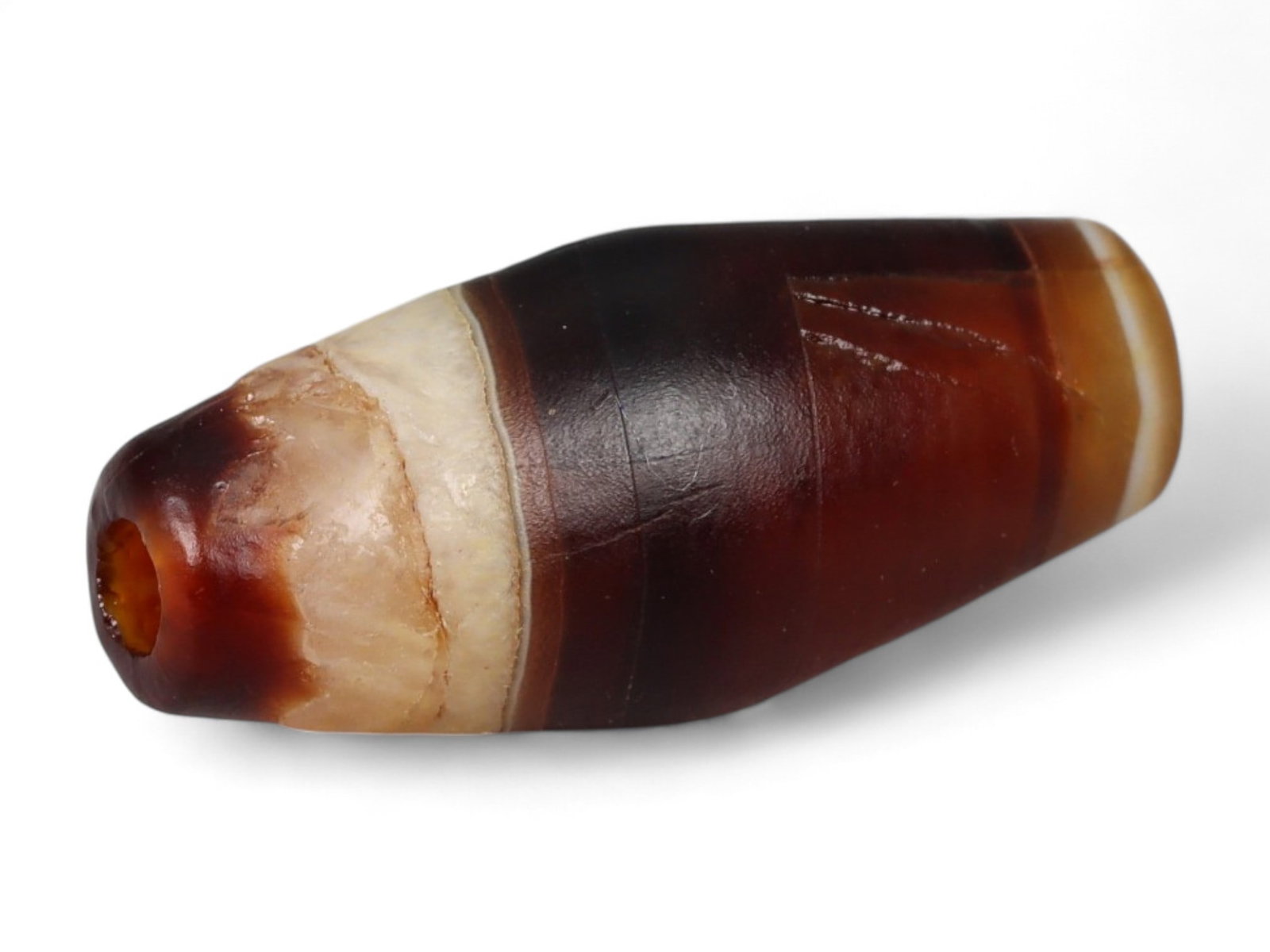Ancient Tibetan Himalayan Banded Agate Dzi Bead, c. 9th-14th Century CE, 2cm: This ancient Tibetan Dzi bead, is carved from richly banded agate, its surface revealing bold layers of deep red, amber, and ivory-white. Its elongated cylindrical form, tapering at the ends, embodies