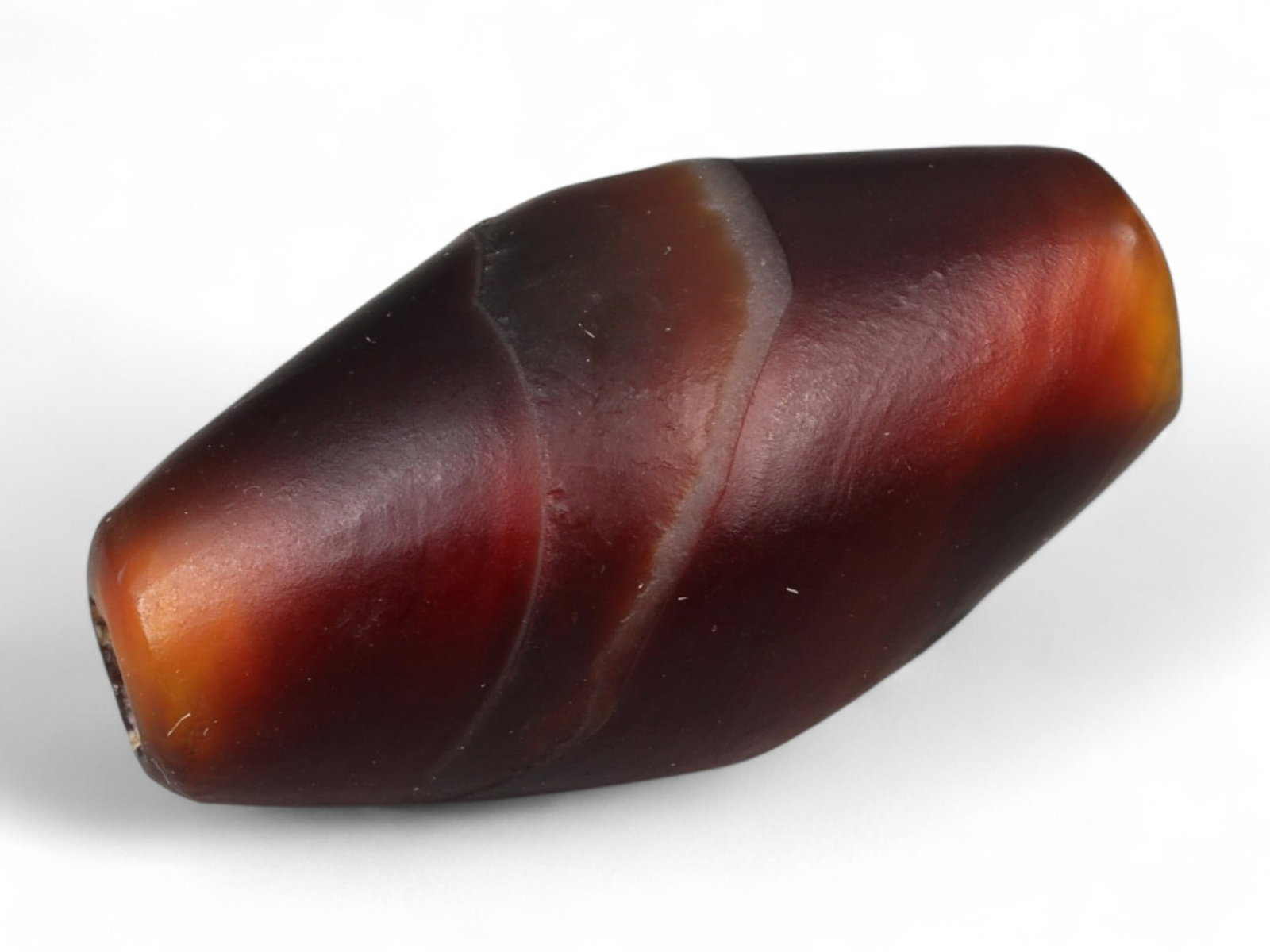 Ancient Tibetan Himalayan Banded Agate Dzi Bead, c. 9th-14th Century CE, 2.3cm: This ancient Tibetan Dzi bead, is carved from richly banded agate, its surface revealing bold layers of deep red, amber, and ivory-white. Its elongated cylindrical form, tapering at the ends, embodies