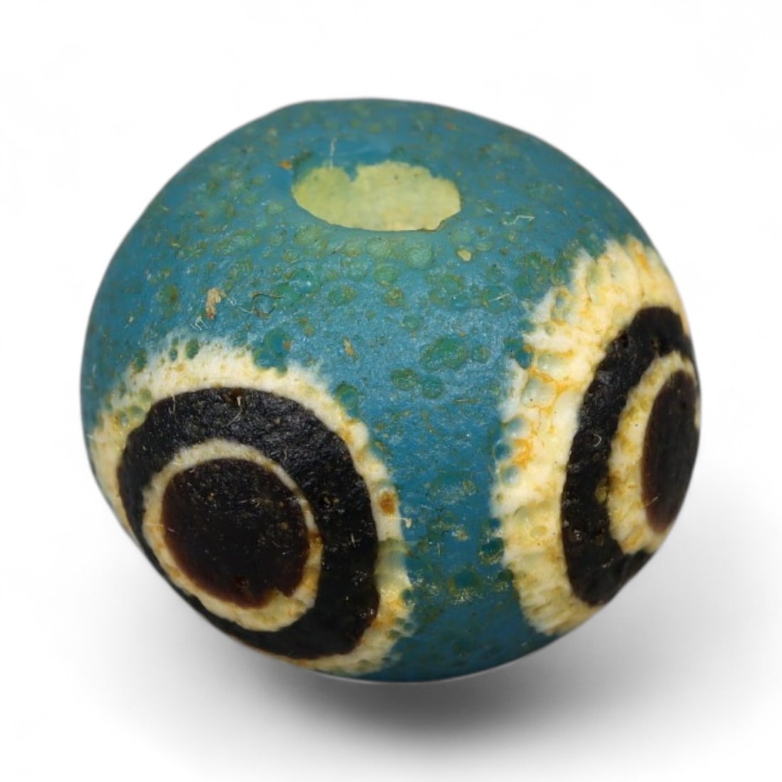 Ancient Roman Stratified Glass Eye Bead, c. 1st-3rd Century CE, 1.2cm: This finely crafted Roman glass eye bead, dating from the 1st to 3rd century CE, measures 1.2 cm in diameter. Formed through stratified layers of colored glass, it displays concentric circular "eye" m