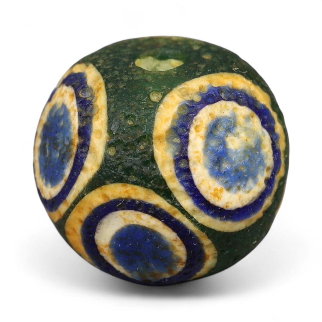 Ancient Roman Stratified Glass Eye Bead, c. 1st-3rd Century CE, 1.2cm: This finely crafted Roman glass eye bead, dating from the 1st to 3rd century CE, measures 1.2 cm in diameter. Formed through stratified layers of colored glass, it displays concentric circular "eye" m