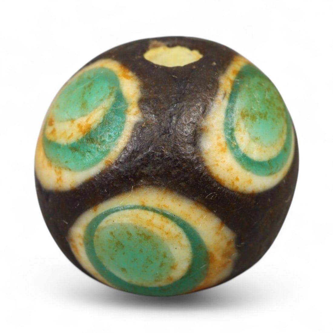 Ancient Roman Stratified Glass Eye Bead, c. 1st-3rd Century CE, 1.2cm: This finely crafted Roman glass eye bead, dating from the 1st to 3rd century CE, measures 1.2 cm in diameter. Formed through stratified layers of colored glass, it displays concentric circular "eye" m
