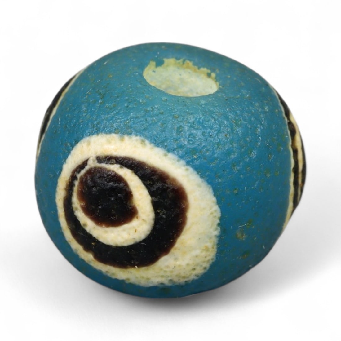 Ancient Roman Stratified Glass Eye Bead, c. 1st-3rd Century CE, 1.2cm: This finely crafted Roman glass eye bead, dating from the 1st to 3rd century CE, measures 1.2 cm in diameter. Formed through stratified layers of colored glass, it displays concentric circular "eye" m
