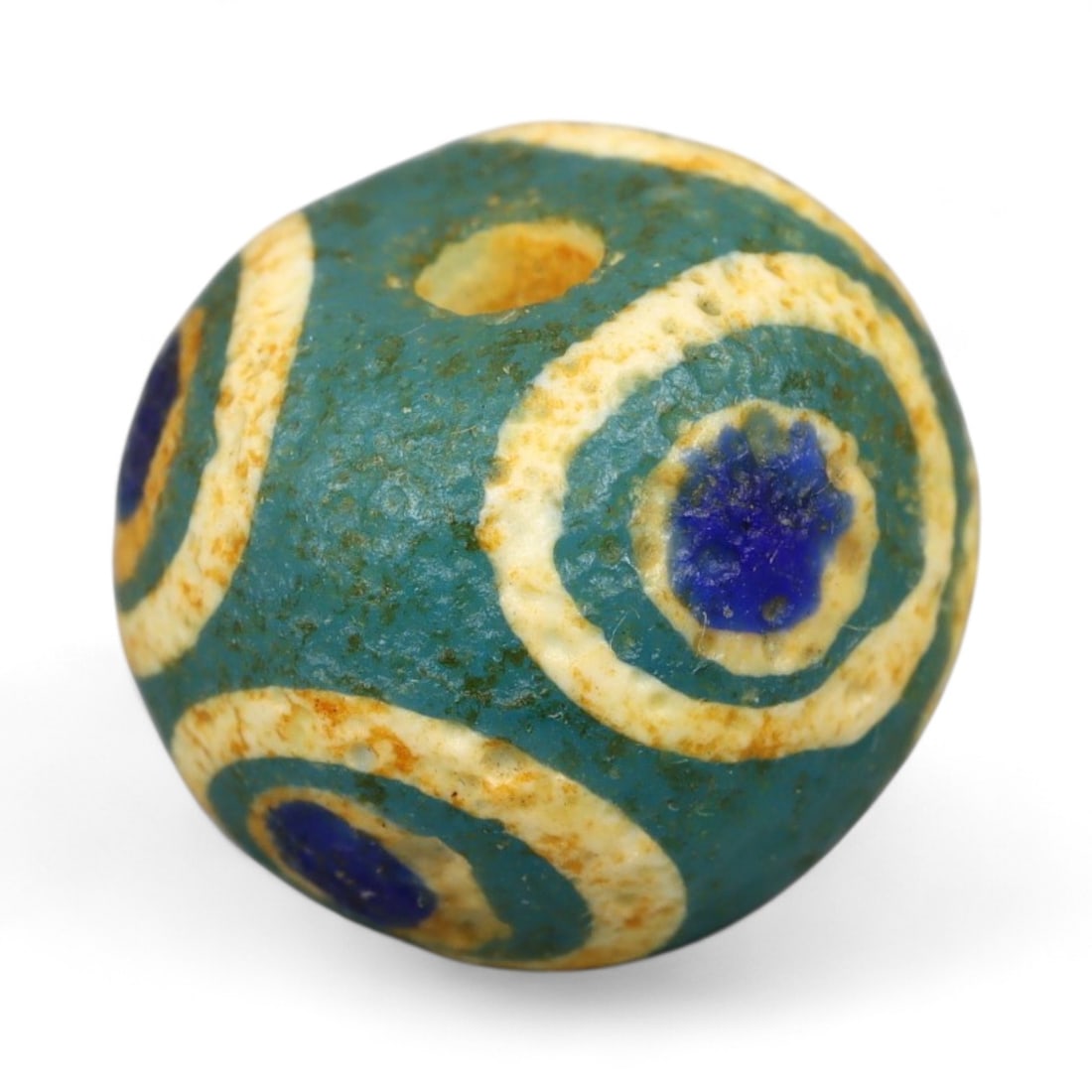 Ancient Roman Stratified Glass Eye Bead, c. 1st-3rd Century CE, 1.2cm: This finely crafted Roman glass eye bead, dating from the 1st to 3rd century CE, measures 1.2 cm in diameter. Formed through stratified layers of colored glass, it displays concentric circular "eye" m