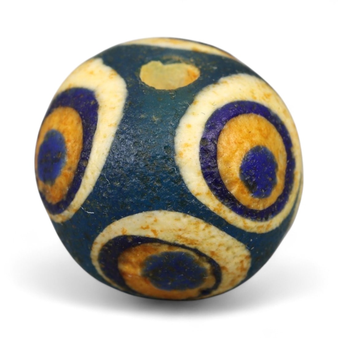 Ancient Roman Stratified Glass Eye Bead, c. 1st-3rd Century CE, 1.2cm: This finely crafted Roman glass eye bead, dating from the 1st to 3rd century CE, measures 1.2 cm in diameter. Formed through stratified layers of colored glass, it displays concentric circular "eye" m