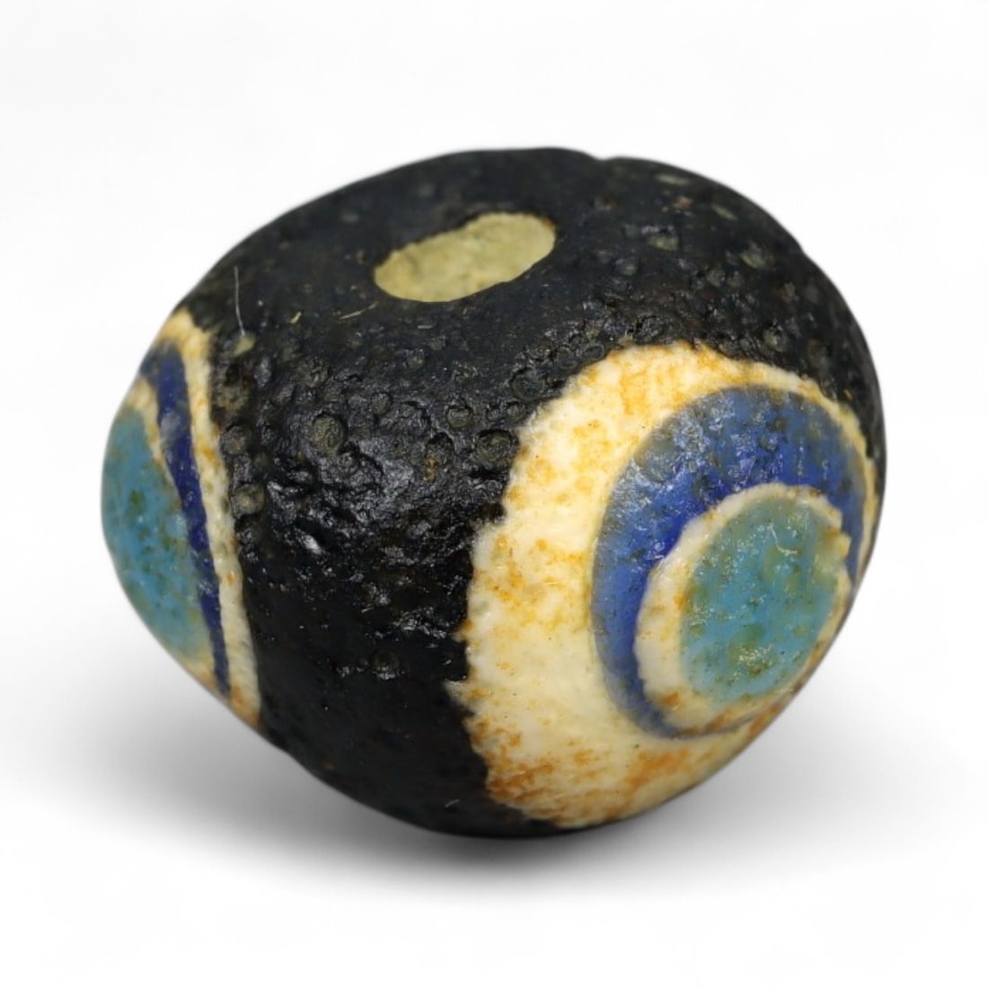 Ancient Roman Stratified Glass Eye Bead, c. 1st-3rd Century CE, 1.2cm: This finely crafted Roman glass eye bead, dating from the 1st to 3rd century CE, measures 1.2 cm in diameter. Formed through stratified layers of colored glass, it displays concentric circular "eye" m