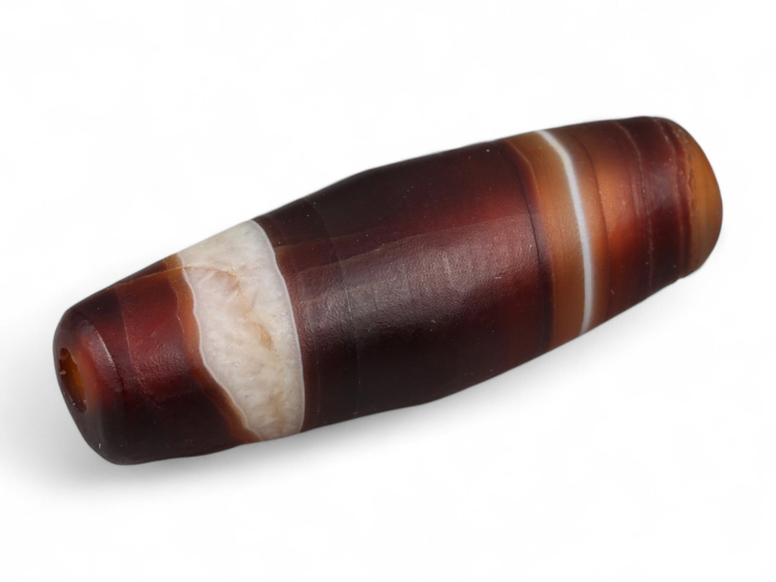 Ancient Tibetan Himalayan Banded Agate Dzi Bead, c. 9th-14th Century CE, 2.2cm: This ancient Tibetan Dzi bead, is carved from richly banded agate, its surface revealing bold layers of deep red, amber, and ivory-white. Its elongated cylindrical form, tapering at the ends, embodies