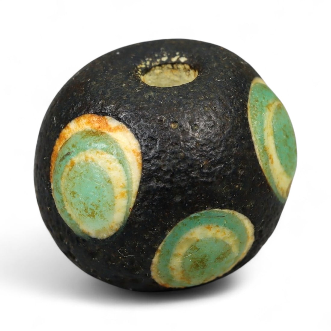 Ancient Roman Stratified Glass Eye Bead, c. 1st-3rd Century CE, 1.2cm: This finely crafted Roman glass eye bead, dating from the 1st to 3rd century CE, measures 1.2 cm in diameter. Formed through stratified layers of colored glass, it displays concentric circular "eye" m