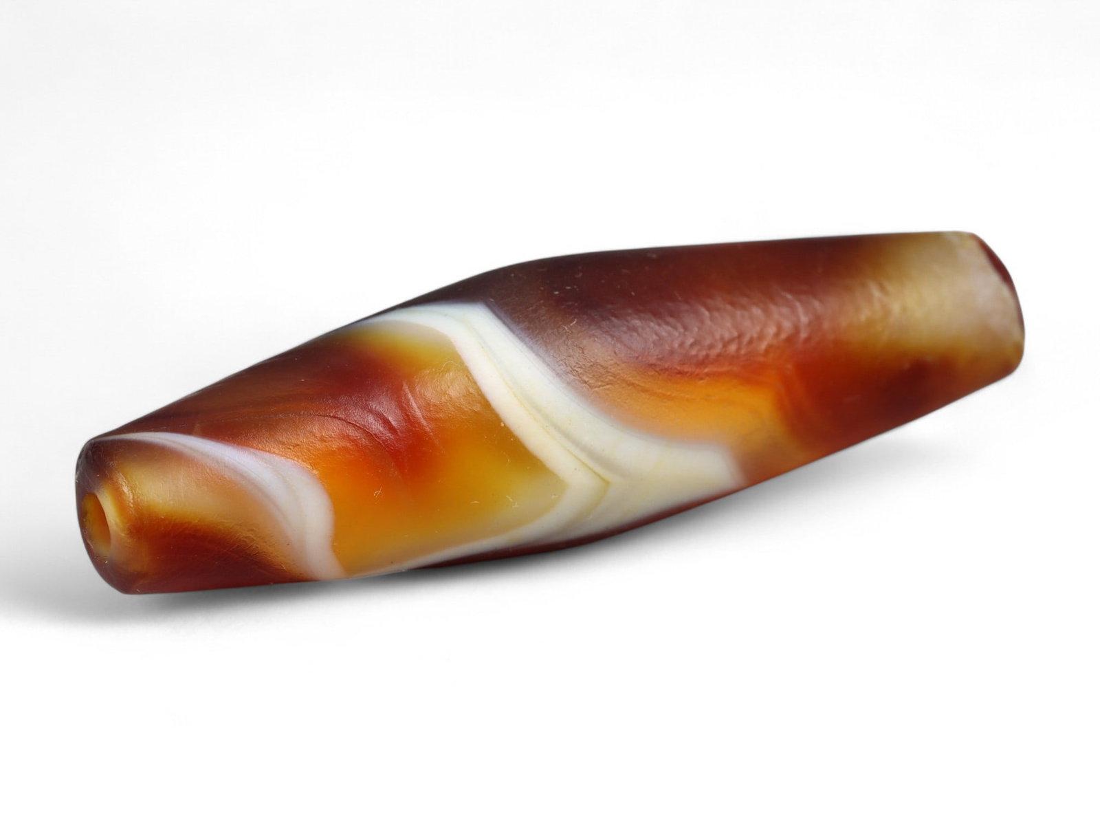 Ancient Tibetan Himalayan Banded Agate Dzi Bead, c. 9th-14th Century CE, 3.5cm: This ancient Tibetan Dzi bead, measuring 2.6 cm, is carved from richly banded agate, its surface revealing bold layers of deep red, amber, and ivory-white. Its elongated cylindrical form, tapering at 