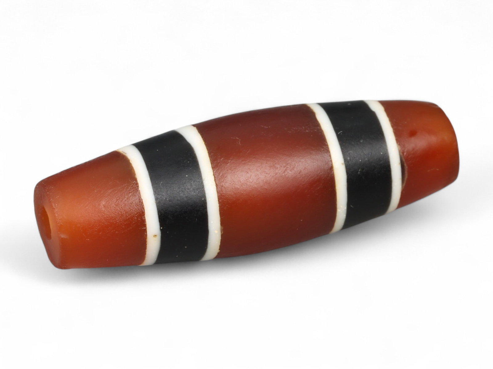 Antique Tibetan Carnelian Agate Banded Bead, c. 20th Century, 3.7cm: This elongated barrel-shaped bead, measuring 3.7cm, is carved from warm carnelian agate and enhanced with bold black and white banded stripes. Its crisp symmetry and high polish mark it as a later Tib