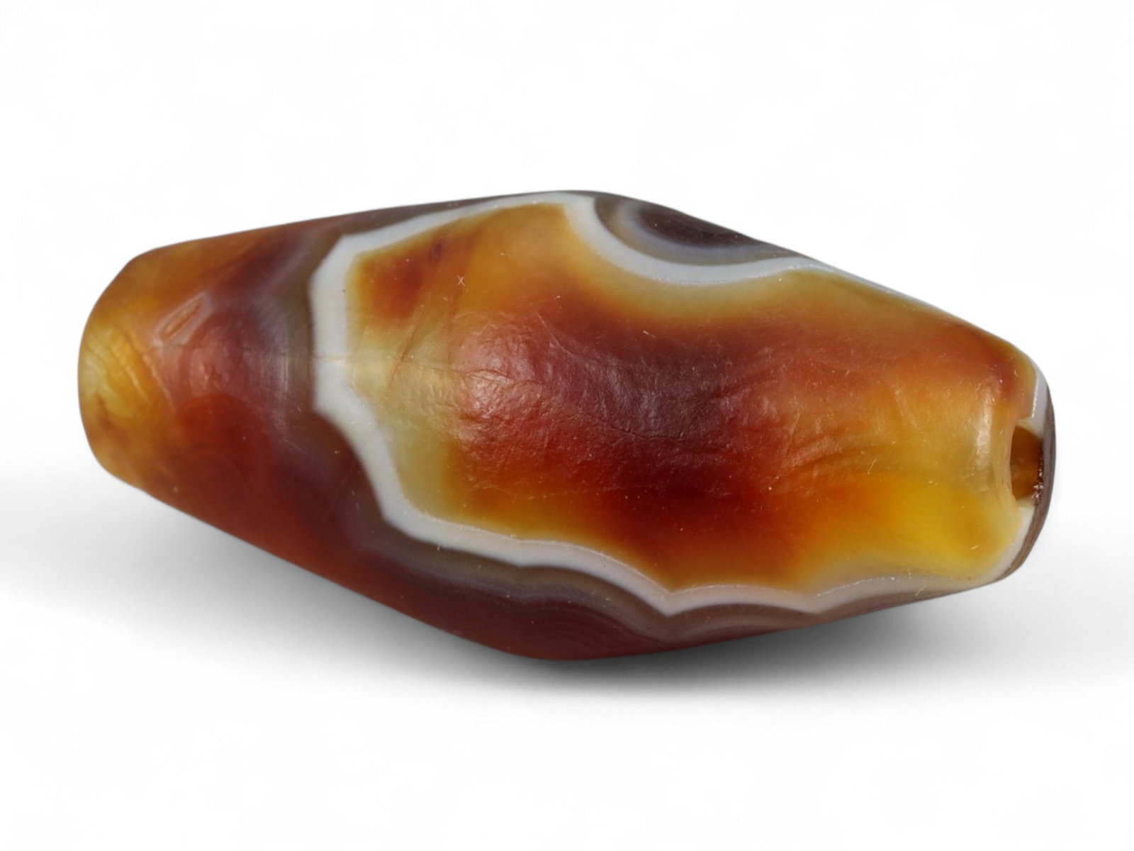 Ancient Tibetan Himalayan Banded Agate Dzi Bead, c. 9th-14th Century CE, 2.2cm: This ancient Tibetan Dzi bead, is carved from richly banded agate, its surface revealing bold layers of deep red, amber, and ivory-white. Its elongated cylindrical form, tapering at the ends, embodies
