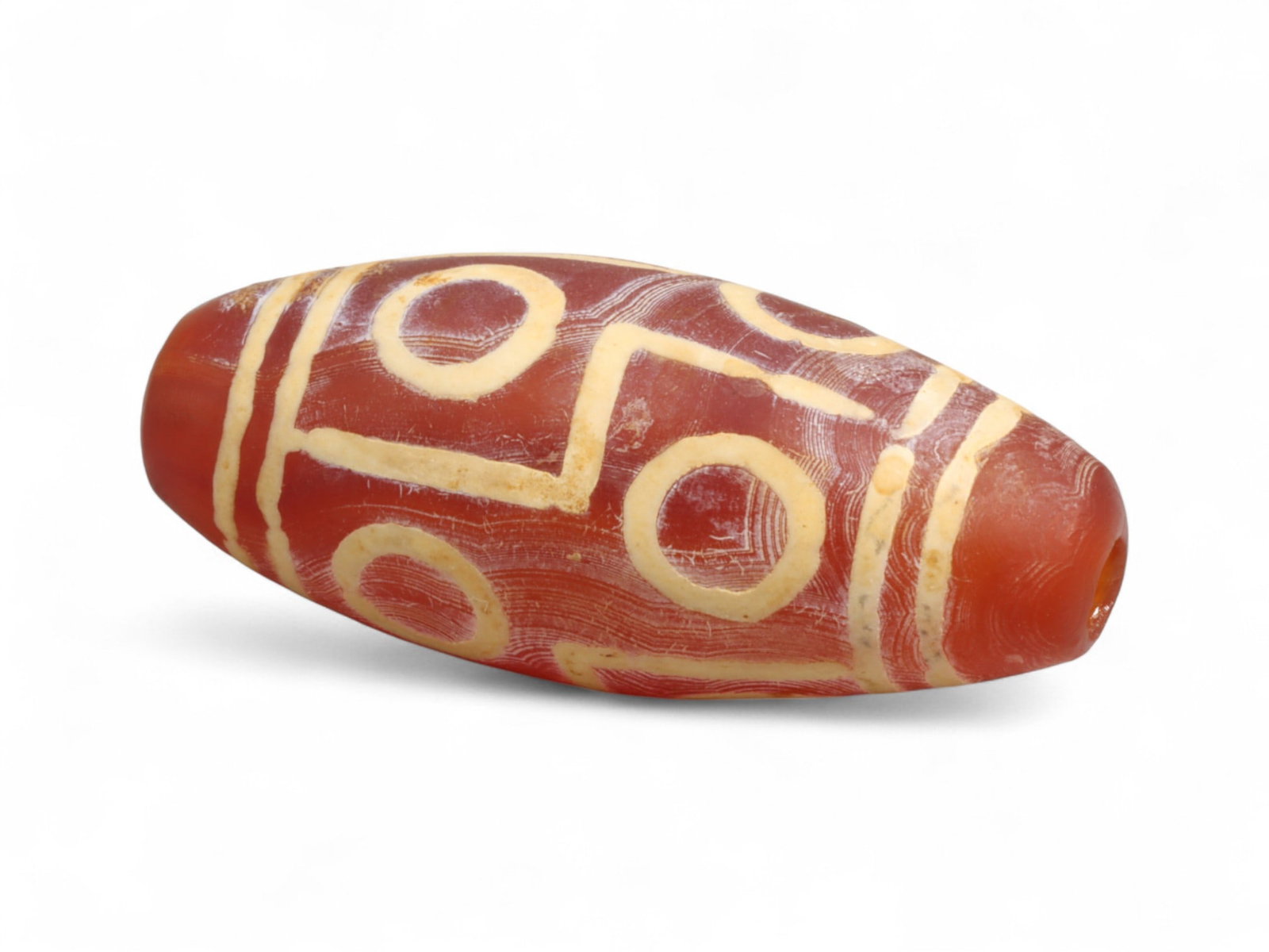 Antique Tibetan Carnelian Etched Dzi-Style Bead, c. 19th-20th Century 3.4cm: This elongated carnelian bead, measuring 3.4 cm (1.33 in), features bold etched designs in creamy white against a deep red-orange ground. The decorative scheme employs concentric circles and linear ba