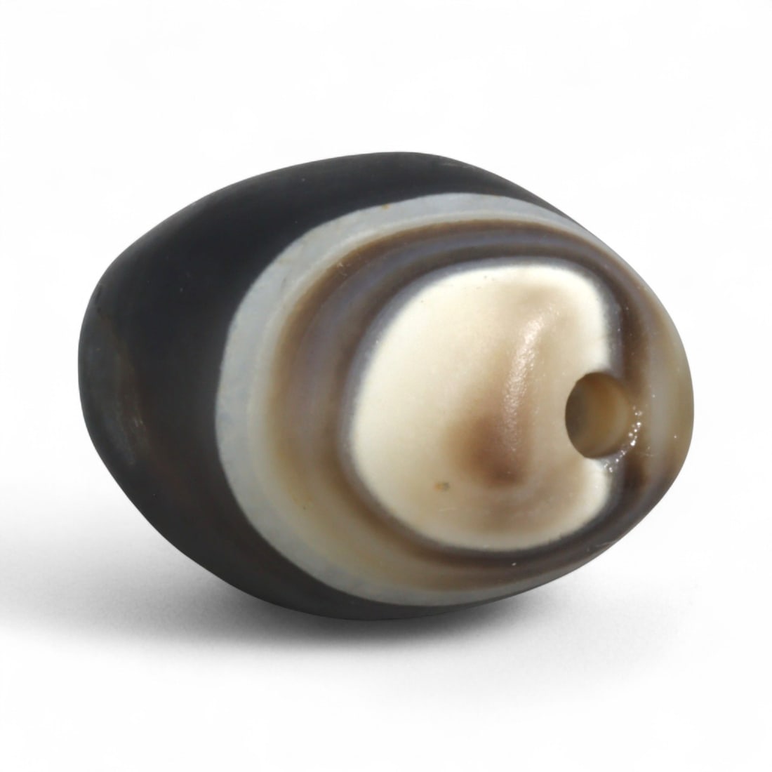 Antique Himalayan Banded Agate Amulet Bead, c. 15th-17th Century, 2cm: This bead, carved from banded agate with smoky brown and gray tones, dates to the Himalayan region between the 15th and 17th centuries. Its elongated oval form, shows concentric layering, a characteri