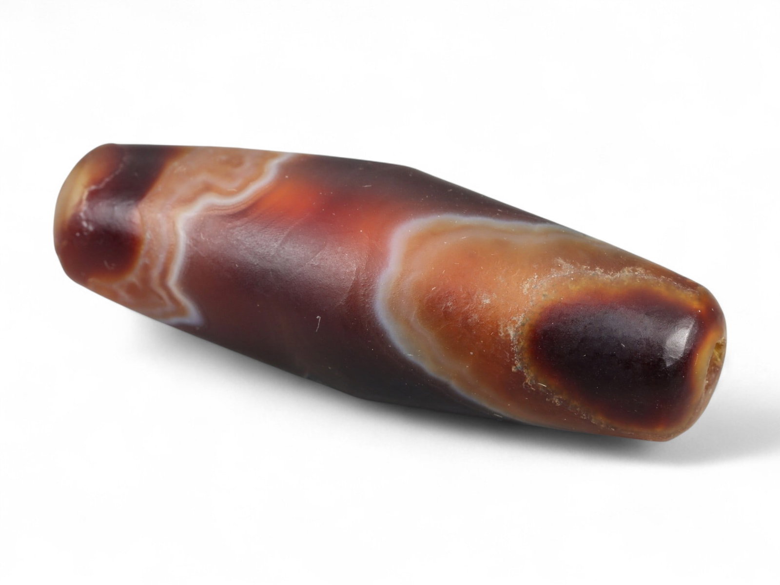 Ancient Tibetan Himalayan Banded Agate Dzi Bead, c. 9th-14th Century CE, 3.5cm: This ancient Tibetan Dzi bead, measuring 2.6 cm, is carved from richly banded agate, its surface revealing bold layers of deep red, amber, and ivory-white. Its elongated cylindrical form, tapering at 