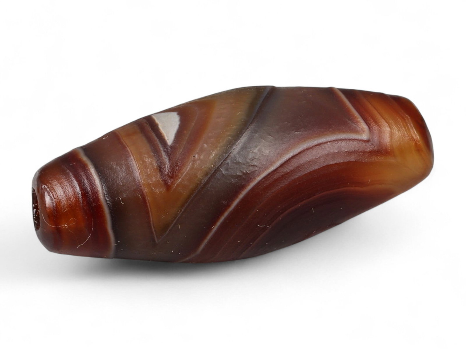 Ancient Tibetan Himalayan Banded Agate Dzi Bead, c. 9th-14th Century CE, 3cm: This ancient Tibetan Dzi bead, is carved from richly banded agate, its surface revealing bold layers of deep red, amber, and ivory-white. Its elongated cylindrical form, tapering at the ends, embodies
