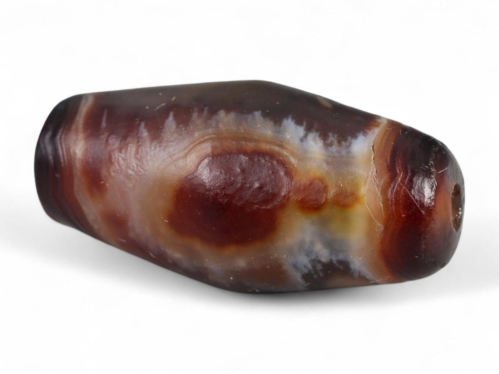 Ancient Tibetan Himalayan Banded Agate Dzi Bead, c. 9th-14th Century CE, 2.5cm: This ancient Tibetan Dzi bead, measuring 2.6 cm, is carved from richly banded agate, its surface revealing bold layers of deep red, amber, and ivory-white. Its elongated cylindrical form, tapering at 