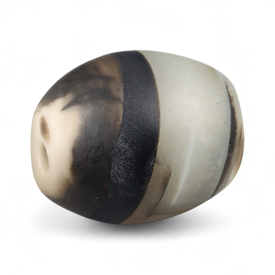 Antique Himalayan Banded Agate Amulet Bead, c. 15th-17th Century, 2.5cm: This bead, carved from banded agate with smoky brown and gray tones, dates to the Himalayan region between the 15th and 17th centuries. Its elongated oval form, shows concentric layering, a characteri