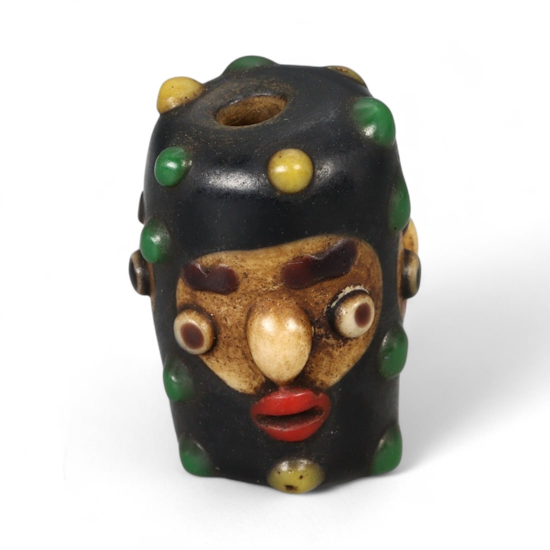 Antique Phoenician Style Multicolored Glass Face Bead, c. 19th-20th Century, 2.5cm: This vibrant antique bead is crafted in the distinctive Phoenician style, featuring a molded human face with applied multicolored details. Its bold design includes protruding eyes, a defined nose, and