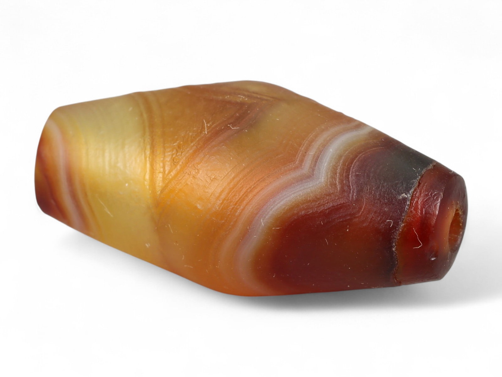 Ancient Tibetan Himalayan Banded Agate Dzi Bead, c. 9th-14th Century CE, 3cm: This ancient Tibetan Dzi bead, measuring 2.6 cm, is carved from richly banded agate, its surface revealing bold layers of deep red, amber, and ivory-white. Its elongated cylindrical form, tapering at 