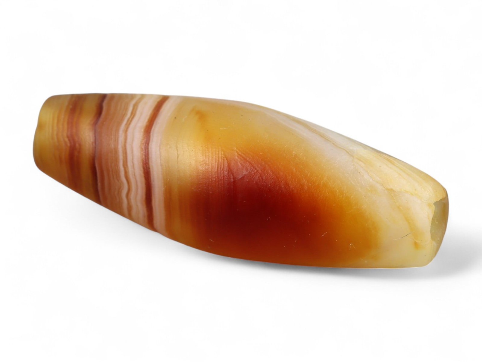 Ancient Tibetan Himalayan Banded Agate Dzi Bead, c. 9th-14th Century CE, 2.5cm: This ancient Tibetan Dzi bead, measuring 2.6 cm, is carved from richly banded agate, its surface revealing bold layers of deep red, amber, and ivory-white. Its elongated cylindrical form, tapering at 