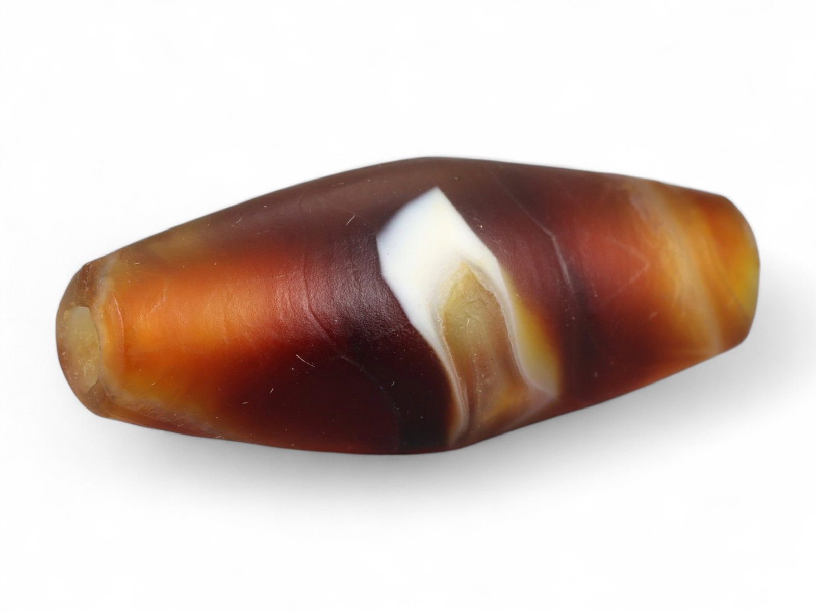 Ancient Tibetan Himalayan Banded Agate Dzi Bead, c. 9th-14th Century CE, 2.5cm: This ancient Tibetan Dzi bead, measuring 2.6 cm, is carved from richly banded agate, its surface revealing bold layers of deep red, amber, and ivory-white. Its elongated cylindrical form, tapering at 