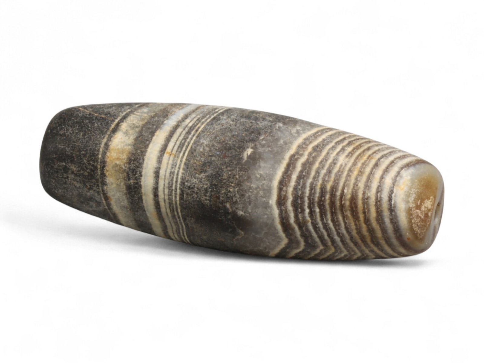 Ancient Medieval Tibetan Striped Agate Barrel Bead, c. 12th-15th Century CE 2.9cm: This elongated barrel bead, was crafted from naturally banded agate during the medieval Tibetan period. Its striking linear and concentric striping, shifting between shades of gray, white, and black, 