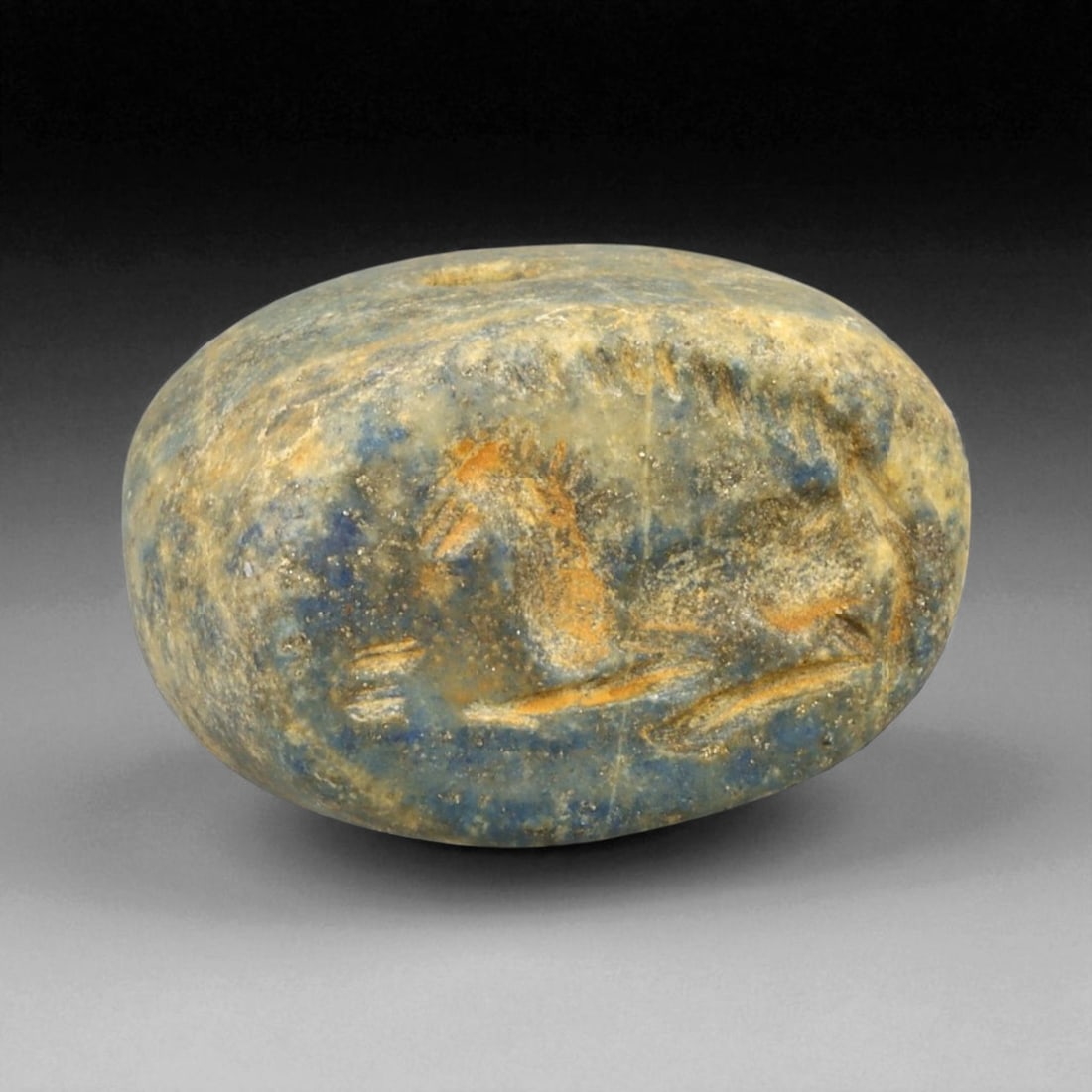 Ancient Mesopotamian Resting Horse Intaglio Amulet in Lapis Lazuli, c. 2nd Millennium BCE, 23g: This evocative amulet, carved from a rich, mottled piece of lapis lazuli, portrays a stylized horse in repose-its slender limbs neatly folded and its arched mane rendered in fine detail. Measuring 2.5