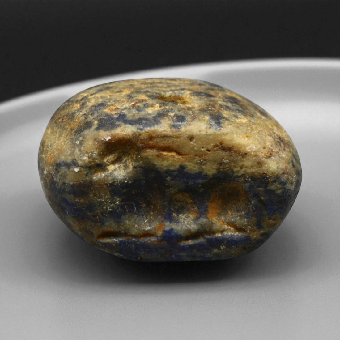 Ancient Elamite Reclining Ibex Lentoid Lapis Lazuli Stamp Seal, c. 2500-1800 BCE, 10.5g: This beautifully domed lentoid stamp seal, carved from variegated lapis lazuli during the Elamite period (c. 2500-1800 BCE), features a stylized reclining ibex with rounded, sculptural form and elegan