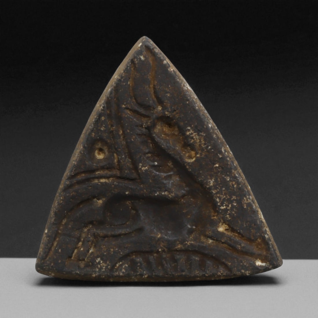 Ancient Near Eastern Triangular Unicorn Motif Stamp Seal, c. 1st Millennium BCE 18g: This unusual triangular stamp seal, measuring 4.5 cm across and weighing 18 grams, is a rare form within the corpus of Ancient Near Eastern glyptic art. Carved from a dark stone, it depicts a stylized