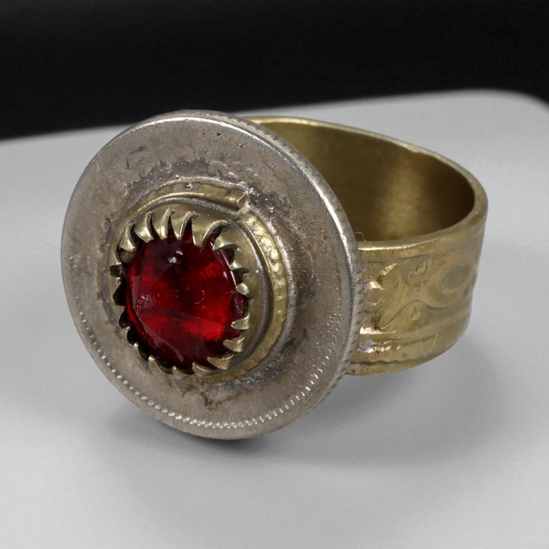 Antique Persian Red Glass Bezel Silver Ring, c. 19th-20th Century 9g: This antique silver ring, dating from the 19th-20th century, showcases a vivid red glass cabochon set within a bold serrated bezel framed by a circular disc. The wide band is engraved with subtle foli