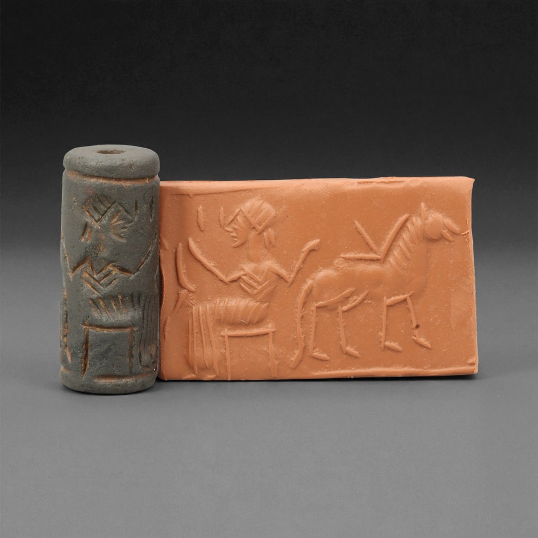 Ancient Akkadian Seated Noble and Equid Motif Hematite Cylinder Seal, c. 2350-2150 BCE, 4.4 cm: This elegant hematite cylinder seal, dating to the Akkadian Empire (circa 2350-2150 BCE), depicts a seated noble or deity facing an equid in a deliberate act of gesture or command. The composition ref