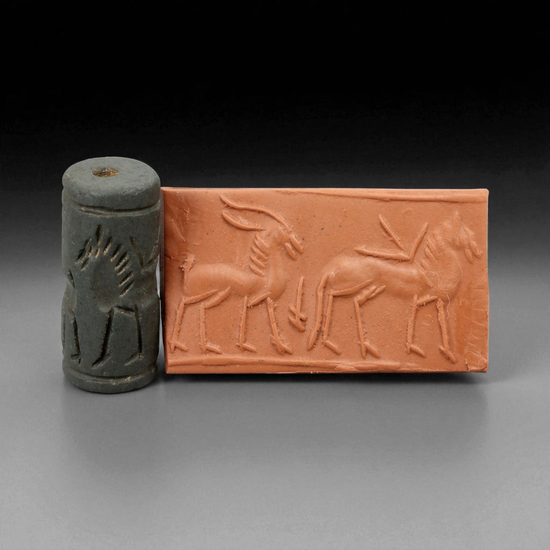 Ancient Early Dynastic Confronted Ibex and Onager Motif Hematite Cylinder Seal, c. 2900-2350 BCE,: This finely executed cylinder seal, carved from dark hematite, originates from the Early Dynastic Period of Sumer (circa 2900-2350 BCE). The design depicts an elegant ibex facing an onager in poised s