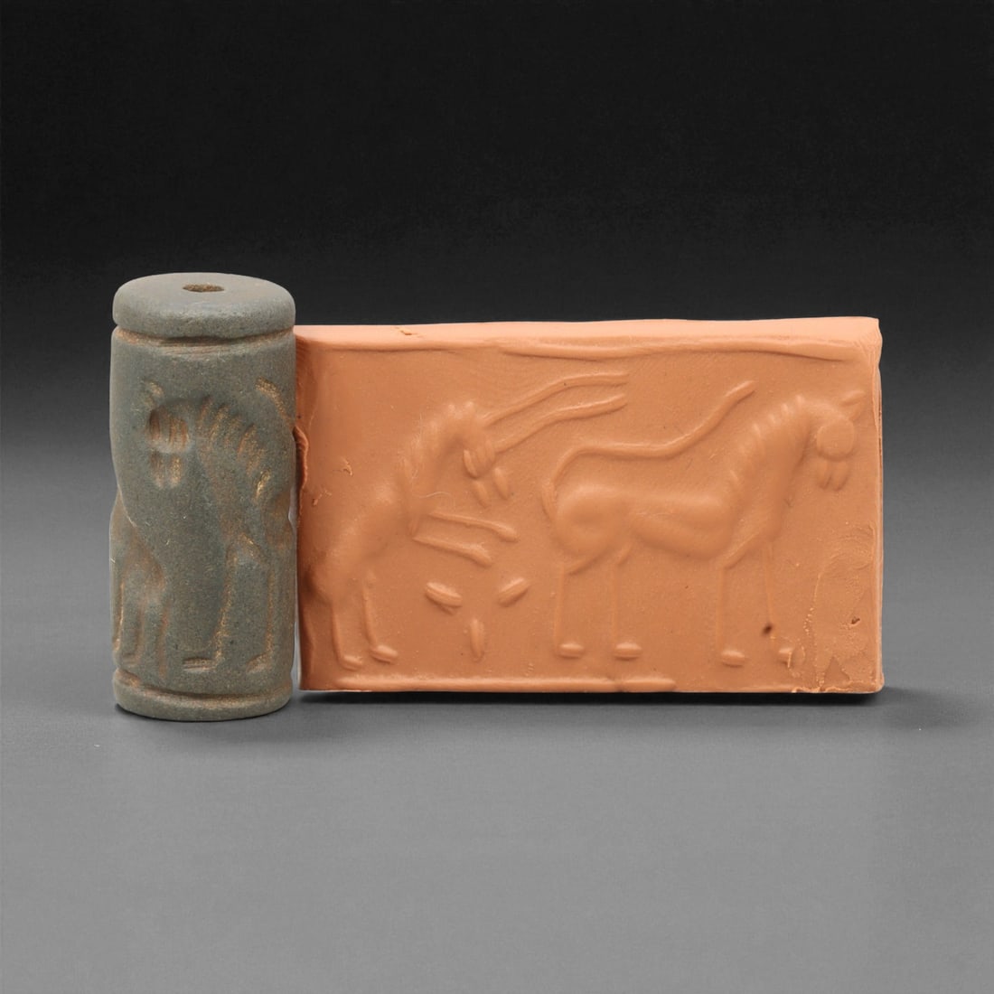 Ancient Early Dynastic Confronted Equids Motif Hematite Cylinder Seal, c. 2900-2350 BCE, 3.9 cm: This finely crafted cylinder seal, carved from dark gray hematite, dates to the Early Dynastic Period of Sumer (circa 2900-2350 BCE). The design presents two equids in confrontation, their elongated b