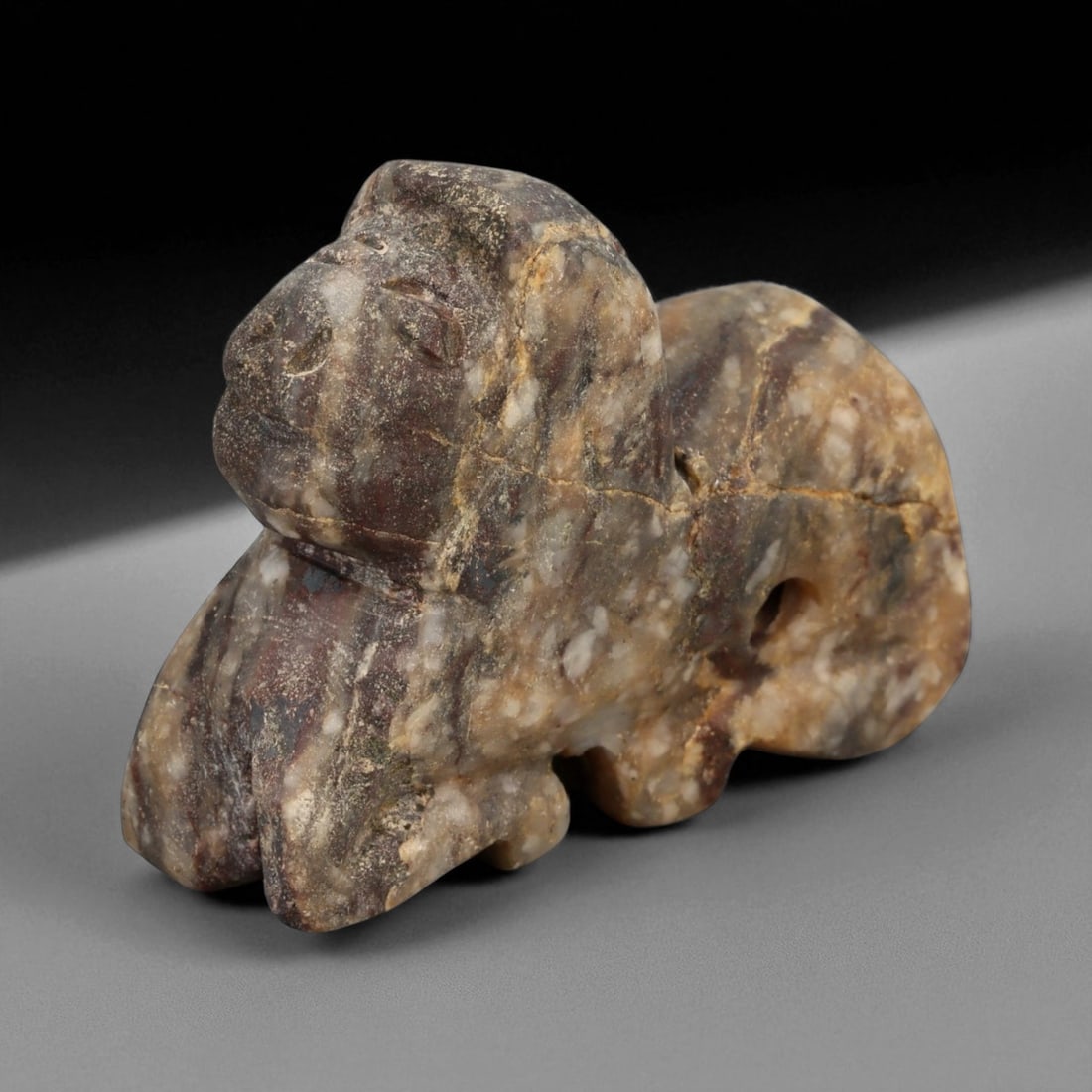 Ancient Elamite Feline Amulet in Banded Stone, c. 2000-1500 BCE, 6cm: This finely sculpted amulet represents a crouching feline, carved from a naturally banded brown and cream stone. Its smooth, rounded contours and minimal facial detailing recall the early Elamite trad