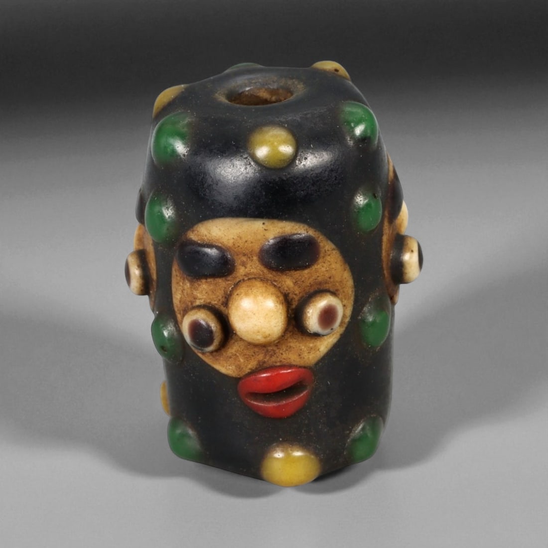 Antique Phoenician-Style Polychrome Glass Face Bead, 19th-20th Century 2.5 cm: This vivid polychrome glass bead, measuring approximately 2.5 cm in height, is a fine antique example inspired by the ancient Phoenician glassmaking tradition. Crafted during the late 19th to early 20